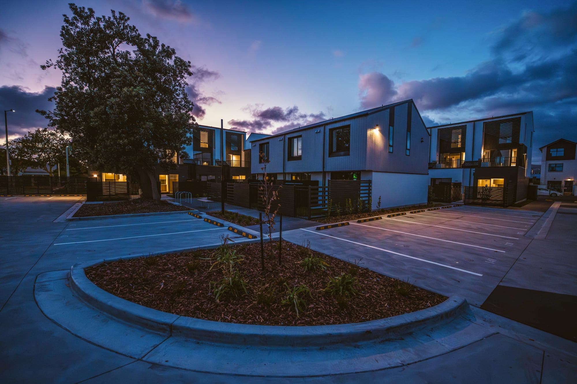 A curved, concrete-kerbed planting island breaking up the parking court, lit at dusk.