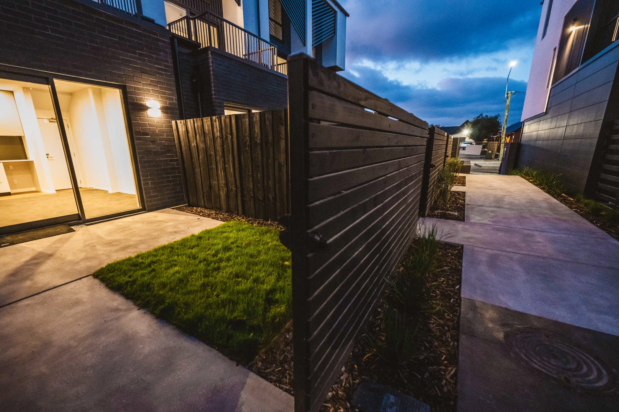 A private courtyard — concrete patio, a neat square of turf and a path running alongside the fence.