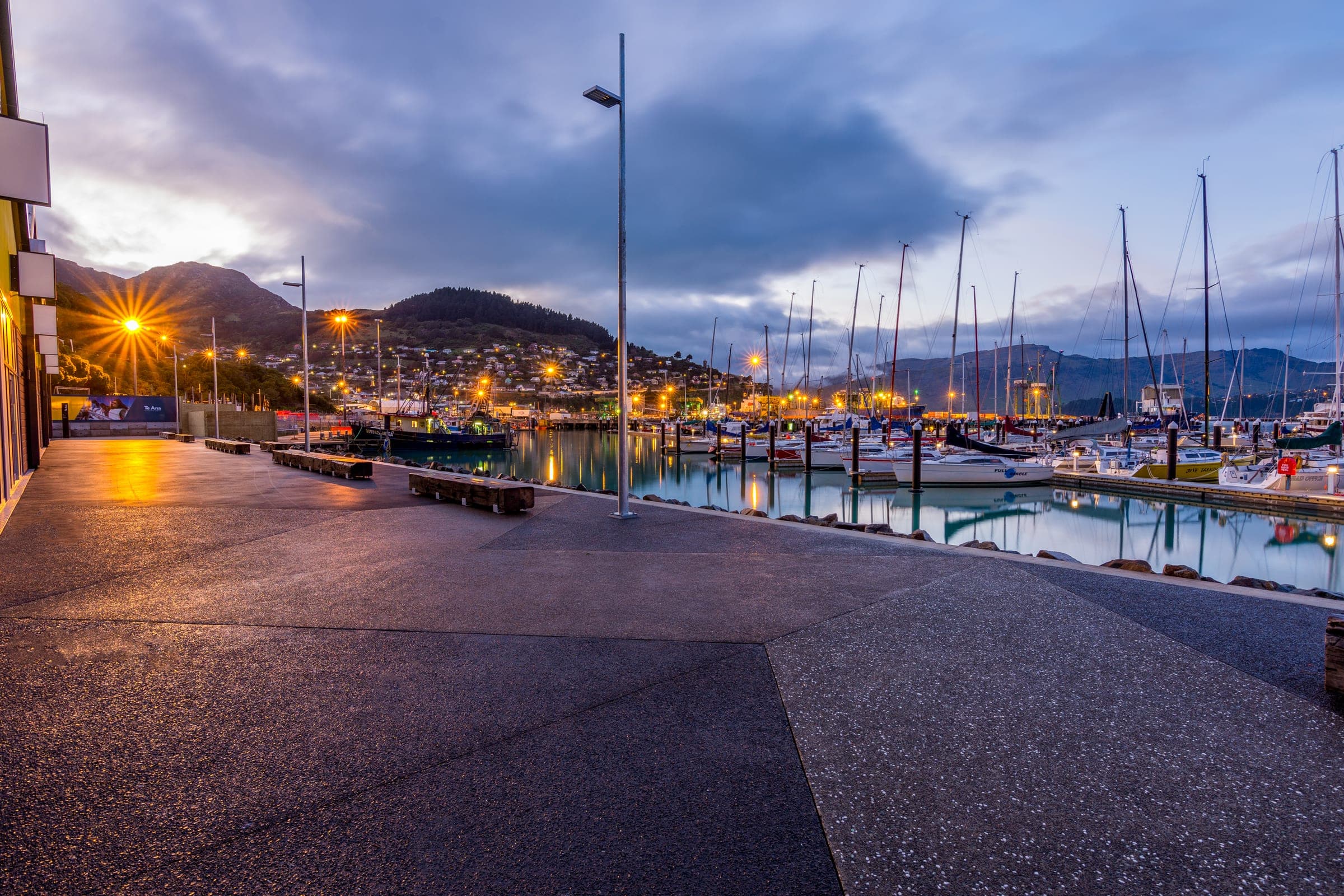 The exposed-aggregate promenade running the length of the marina edge at dusk.
