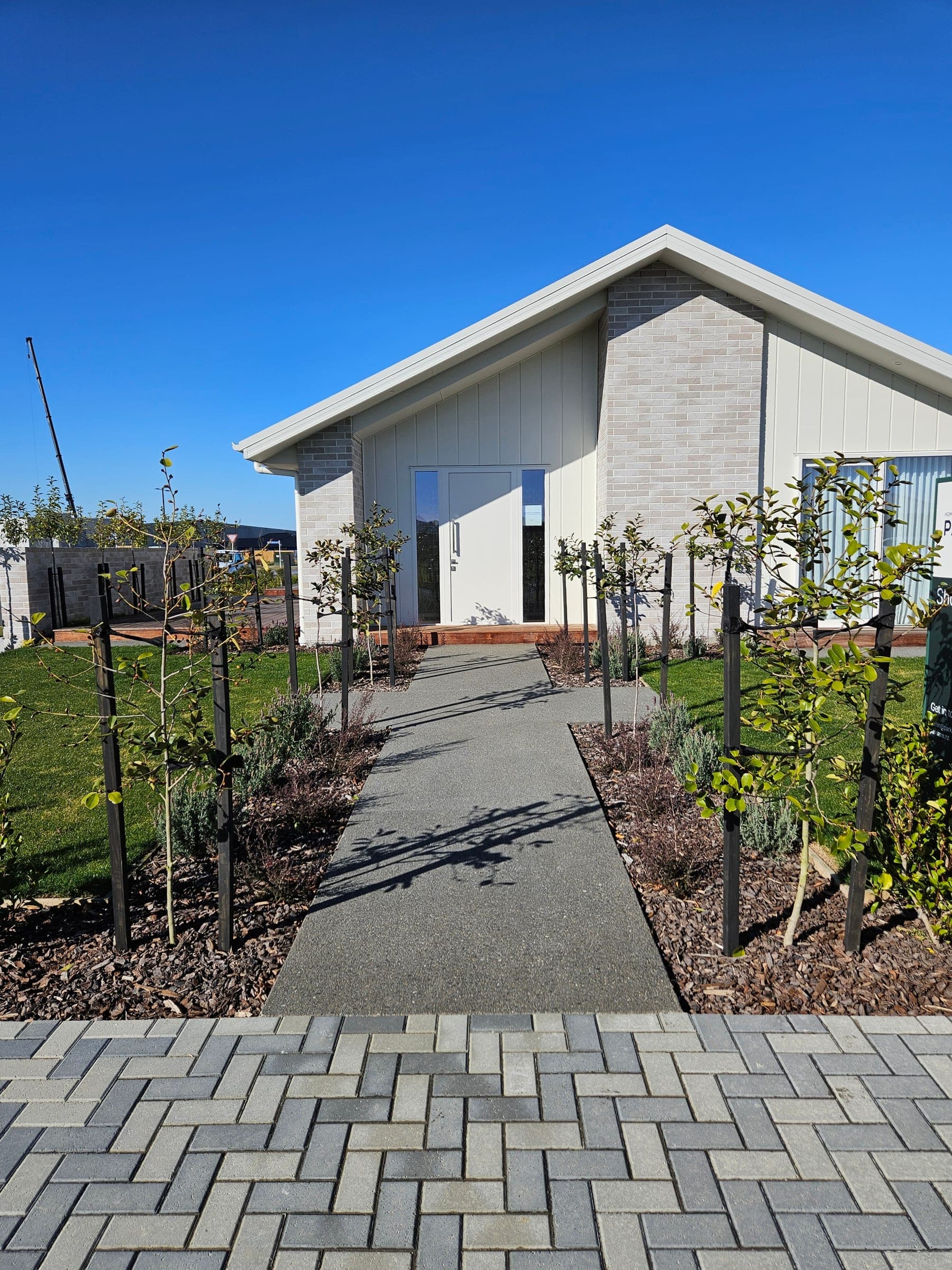 Exposed-aggregate entry path and herringbone paver courtyard, framed by the gardens.