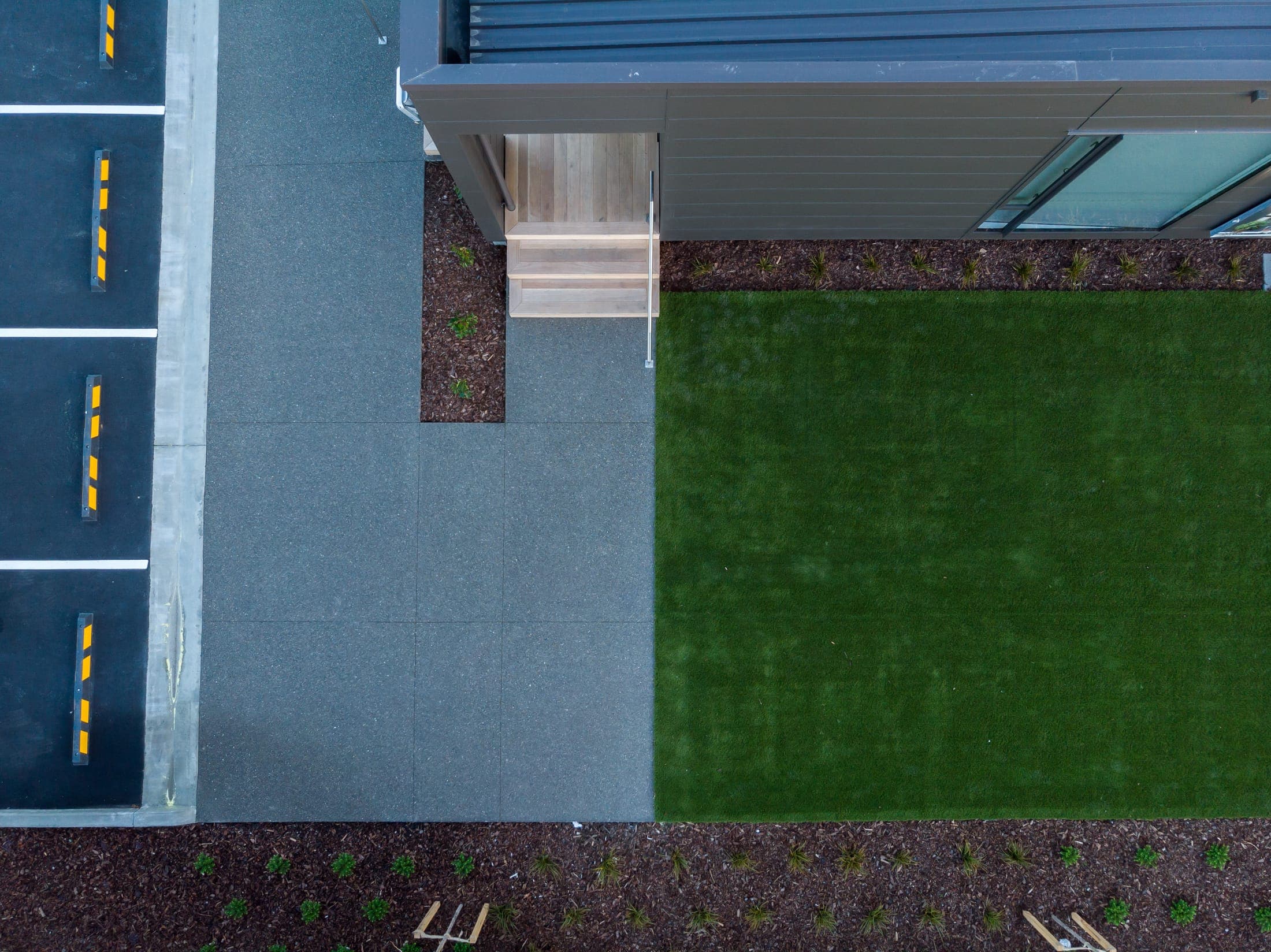 Exposed-aggregate apron meeting the lawn and timber entry step, saw-cut into neat panels.
