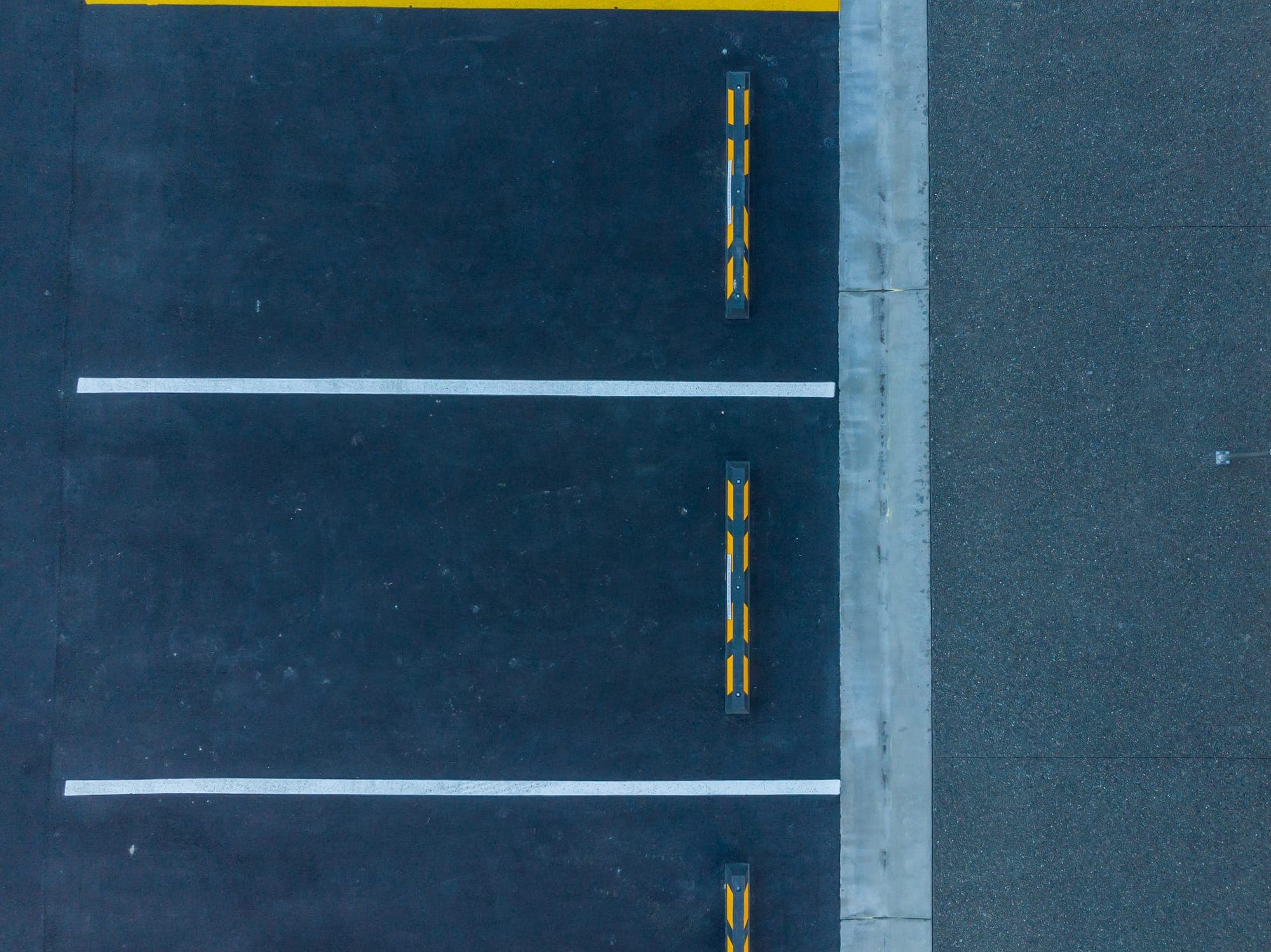 Line-marked parking bays and wheel stops, bounded by a crisp concrete kerb and exposed-aggregate edge.